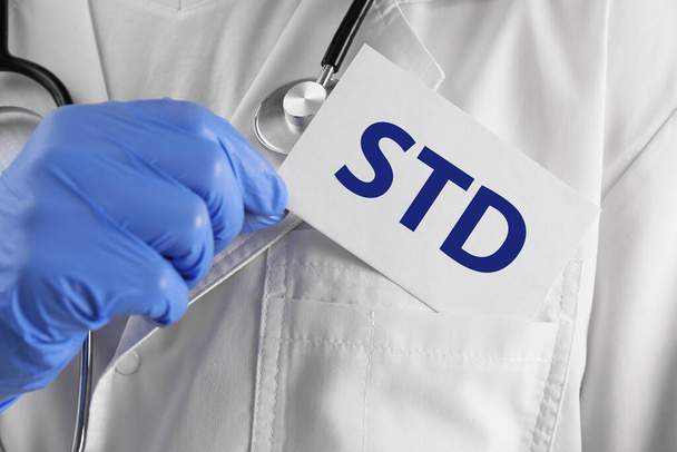 Doctor holding sheet of paper with abbreviation STD, closeup - Foto, Bild