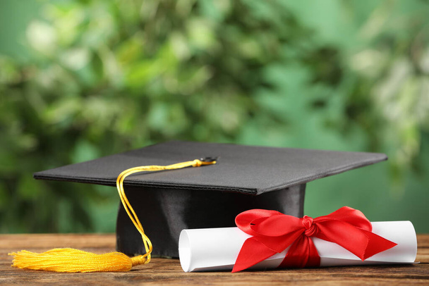 Graduation hat and diploma on wooden table against blurred background, space for text - Φωτογραφία, εικόνα