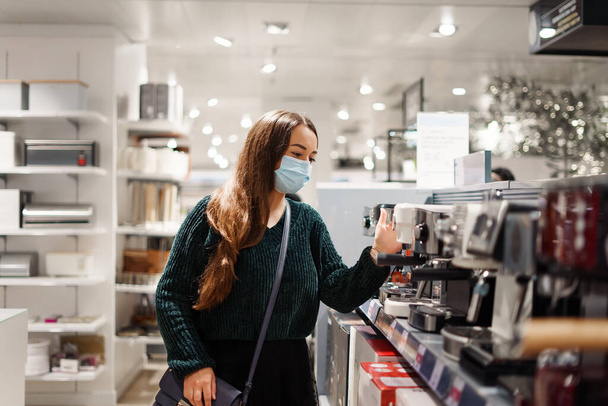 顔のマスクの陽気な女性は、 covid19パンデミックの間にショッピングモールでコーヒーマシンを選択します - 写真・画像