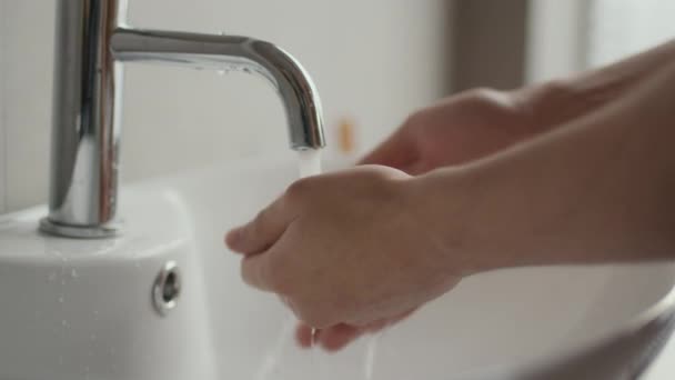 Lähikuva nuori tunnistamaton valkoihoinen mies pestä kädet pesuallas veden alla, hidastettuna - Materiaali, video