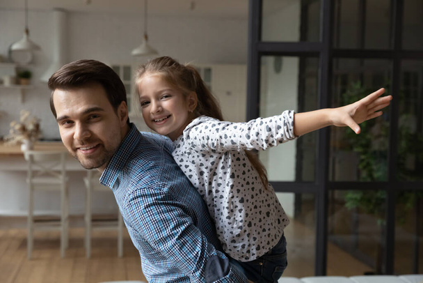 Portrait smiling Caucasian father piggy backing 8s daughter pretending flying - Foto, afbeelding