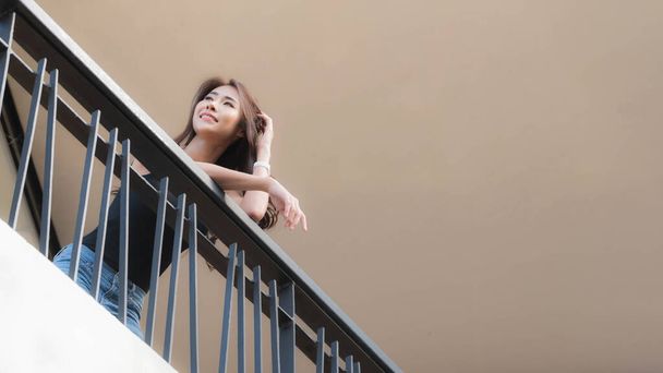 Beautiful woman is leaning on the railing of the balcony looking into the distance. Worm's-eye view. - Фото, изображение