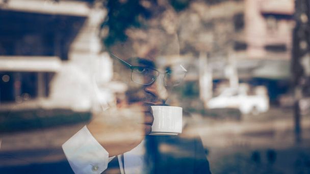 african american businessman drinking hot coffee by window in coffee shop - 写真・画像