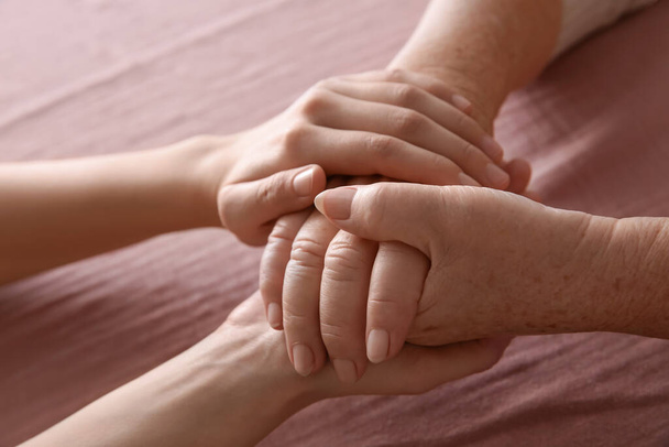 Young and elderly women holding hands together on pink fabric, closeup - Foto, Imagem