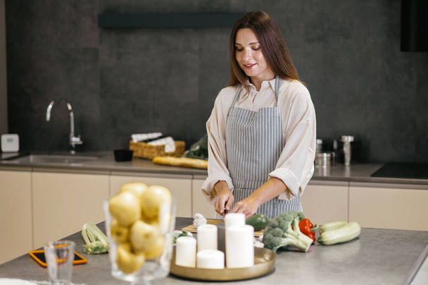 Young woman in apron cutting veggies in the kitchen - Фото, зображення