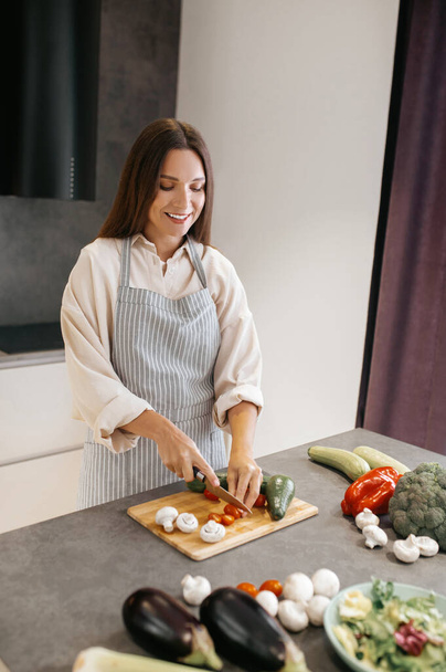 Young woman in apron cutting veggies in the kitchen - Photo, Image