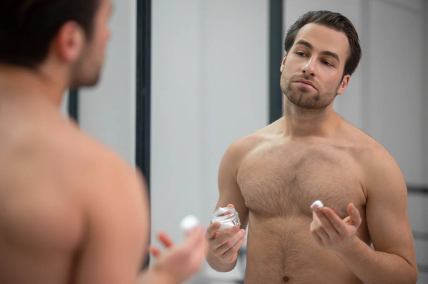 Half-naked man standing near at the mirror and applying shaving foam on his face - Foto, Bild