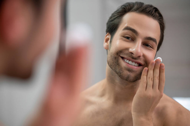 Half-naked man standing near at the mirror and applying shaving foam on his face - Φωτογραφία, εικόνα