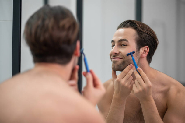 Young man shaving at the mirror - Fotoğraf, Görsel
