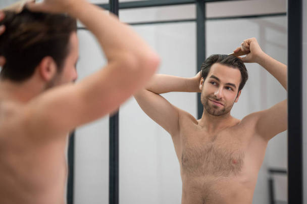 Dark-haired man brushing his hair at the mirror - Foto, Bild