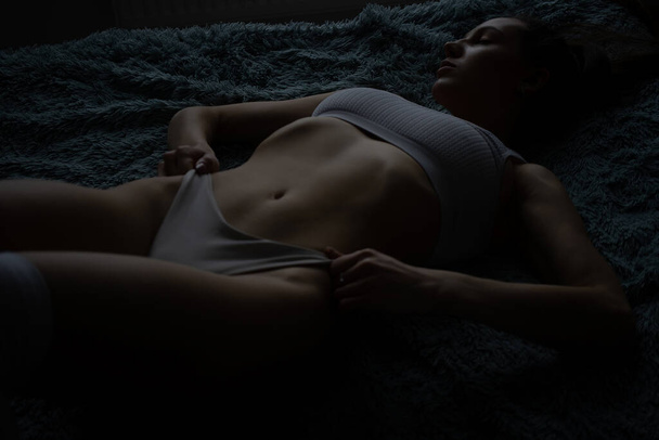 Αισθησιακό νεαρό λεπτό μακρυμάλλη μελαχρινή με γυμνό στήθος φορώντας σέξι δαντελένια εσώρουχα αγγίζοντας το σώμα προκλητικά στο κρεβάτι και στην πόρτα του υπνοδωματίου - Φωτογραφία, εικόνα