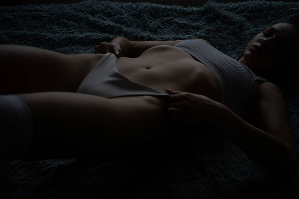 Sensual joven delgada morena de pelo largo con el pecho desnudo usando bragas de encaje sexy tocando el cuerpo provocativamente en la cama y en la puerta del dormitorio - Foto, imagen