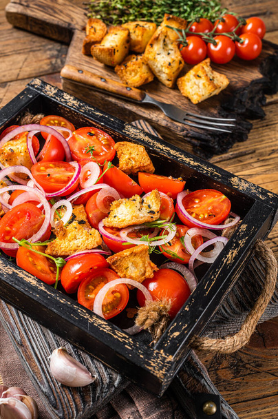 Tradycyjna włoska sałatka Panzanella z pomidorami, cebulą i pieczywem grzankami w drewnianej tacy. Drewniane tło. Widok z góry - Zdjęcie, obraz