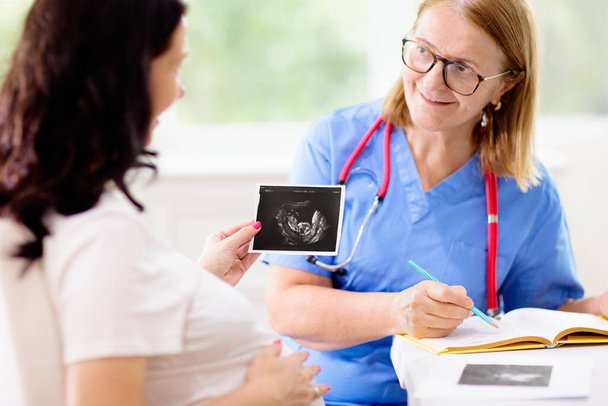 Doctor examining pregnant woman. Pregnancy check. Young Asian female at gynecologist office for prenatal exam. Ob gyn showing patient baby sonogram. Obstetrics and gynecology office. - Foto, Bild