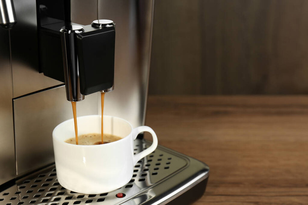 Modern espresso machine pouring coffee into cup on wooden table, closeup. Space for text - Foto, Imagem