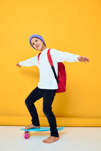 felice scolaro in un maglione bianco skateboard intrattenimento colore giallo sfondo - Foto, immagini
