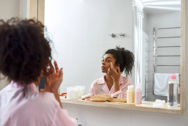 Mujer negra aplicando crema cosmética en su cara - Foto, imagen