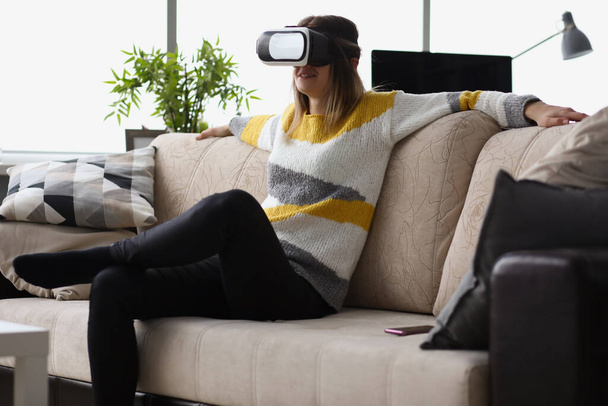 Female sit on couch wear vr glasses modern device at home and enjoy spare time - Foto, imagen