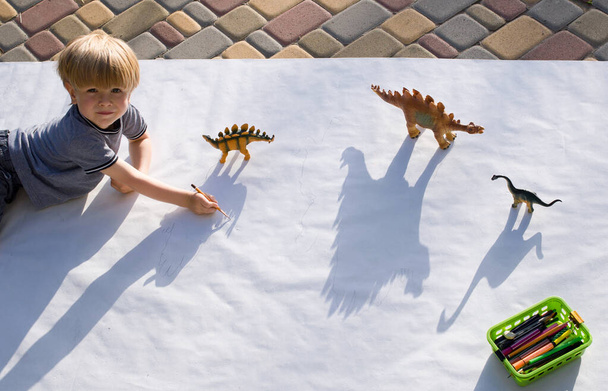 niño dibuja con un lápiz contrastando sombras de dinosaurios de juguete. dibujar un preescolar, ideas creativas para la creatividad de los niños. Actividades interesantes para el desarrollo de los niños - Foto, Imagen