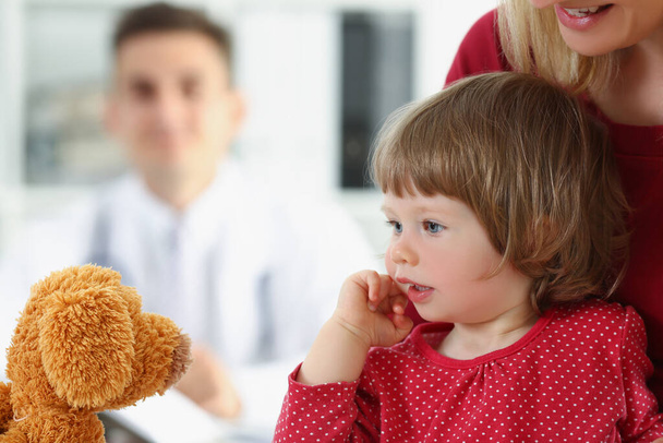 Niña con madre jugar con oso de peluche antes de la cita con el médico - Foto, imagen