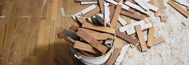 Craftsman in workwear removes the parquet flooring and fills the buckets with the wooden slats during the house renovation process. - Photo, Image