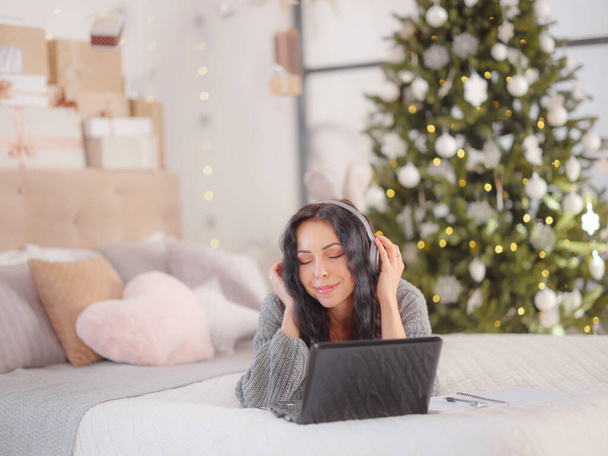 γυναίκα σε άνετο γκρι πλεκτό πουλόβερ χρησιμοποιώντας φορητό υπολογιστή στο κρεβάτι, Χριστούγεννα διακοπές - Φωτογραφία, εικόνα