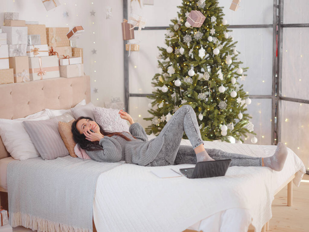 Nainen kodikas harmaa neulotut villapaita kannettavan tietokoneen sängyllä, joulu loma - Valokuva, kuva