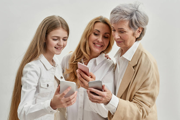 Smiling three females use and watch smartphones - Zdjęcie, obraz