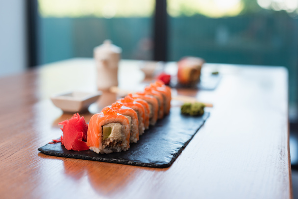 deliciosos rollos de sushi cerca de jengibre en plato negro y mesa de madera, fondo borroso - Foto, Imagen
