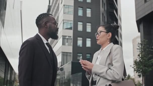 Tracking shot of African-American and Asian businessman and businesswoman in formal wear standing on street and having conversation - Metraje, vídeo
