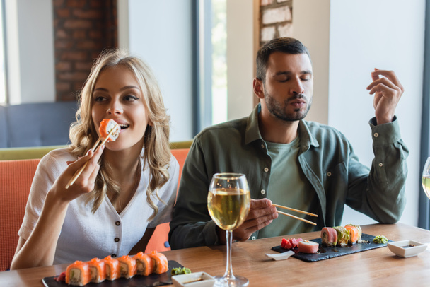 homme avec les yeux fermés profiter de délicieux sushi près de petite amie souriante  - Photo, image