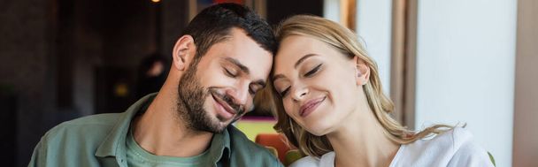 mladý pár usmívá se zavřenýma očima, zatímco sedí hlava k hlavě v kavárně, banner - Fotografie, Obrázek