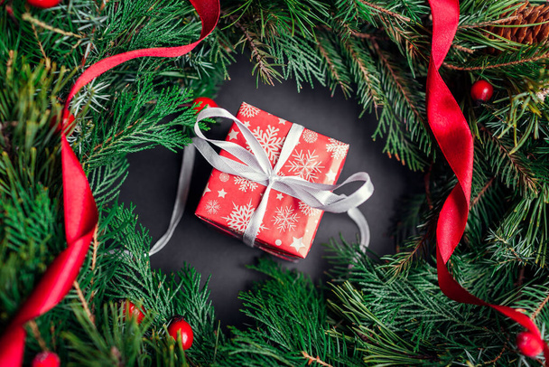 Karácsonyi és újévi piros ajándék doboz csomagolva ünnepi papír és szalag belül fenyő koszorú szalaggal. Ajándék a téli ünnepekre, fekete háttérrel. Felülnézet - Fotó, kép