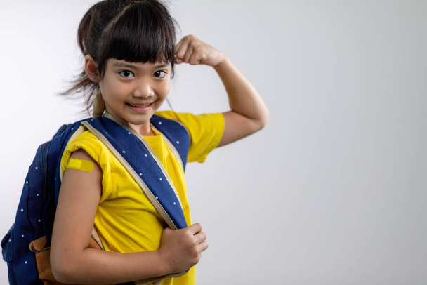  Asian young girl showing her arm with yellow bandage after got vaccinated or inoculation, child immunization, covid delta vaccine concept - Foto, Bild