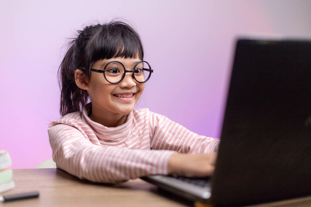 Chica asiática sentada y estudiando en casa en una computadora portátil para estudiar desde casa durante el bloqueo pandémico de Covid-19. Educación en línea, Educación en el hogar - Foto, Imagen
