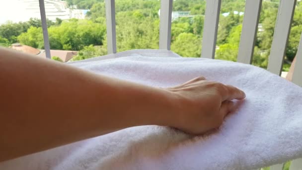 4k βίντεο, κοντινό πλάνο του χεριού μιας γυναίκας αγγίζοντας ένα μαλακό λευκό πετσέτα terry στο μπαλκόνι, με φόντο τη θάλασσα και το πάρκο - Πλάνα, βίντεο