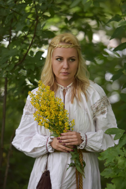 blond vrouw in een wit slavisch shirt tussen het groen in de zomer - Foto, afbeelding