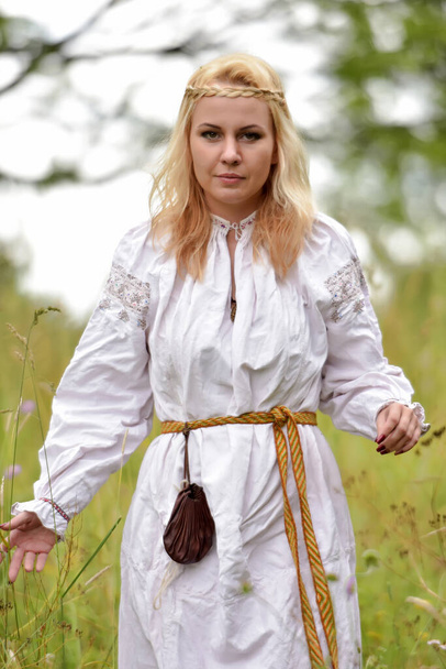 blonde woman in a white slavic shirt among the greenery in summer - Foto, imagen