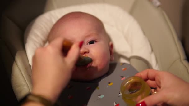 Mother giving food to baby boy, puree from spoon in highchair at home. Complementary infant feeding. - Filmati, video