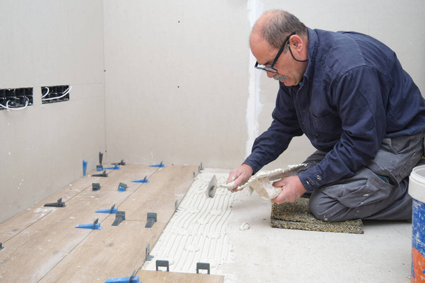Tiler putting tiles adhesive to the floor with the trowel and notched trowel. - Foto, immagini