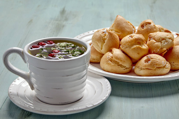 Appetizing profiteroles with whipped cream and a cup of herbal tea - Фото, зображення