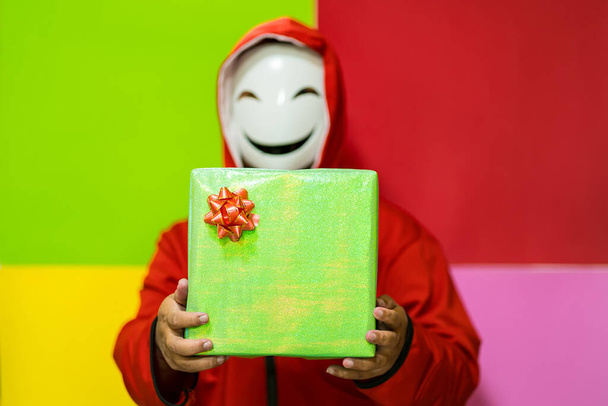 Μπανγκόκ, Ταϊλάνδη - Δεκέμβριος, 18, 2021: Άγνωστος άνθρωπος όνομα φορώντας μια χαμογελαστή μάσκα στέκεται κρατώντας δώρα κουτί.. - Φωτογραφία, εικόνα