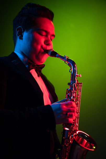 Cute Guy Musician Enjoys Playing the Saxophone, Tenor Saxophone. Neon Light. Close-up Portrait - Foto, Imagem