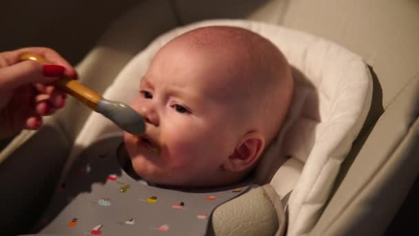 Mother giving food to baby boy, puree from spoon in highchair at home. Complementary infant feeding. - Footage, Video
