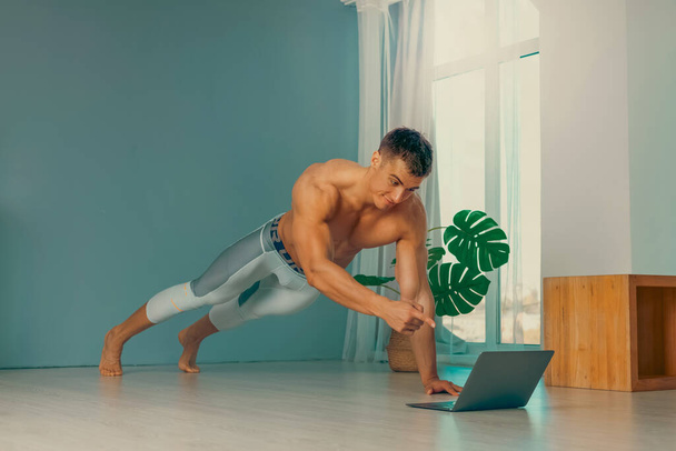 Online trainer. On-line sports. fitness and healthy lifestyle concept. Man with laptop computer doing plank exercise at home during a pandemic. - Photo, Image