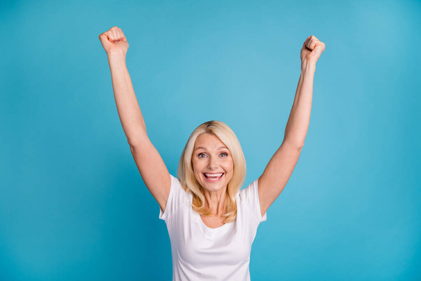 Photo of delighted old woman lucky win raise fists scream wear good look clothes isolated over blue color background - Foto, afbeelding