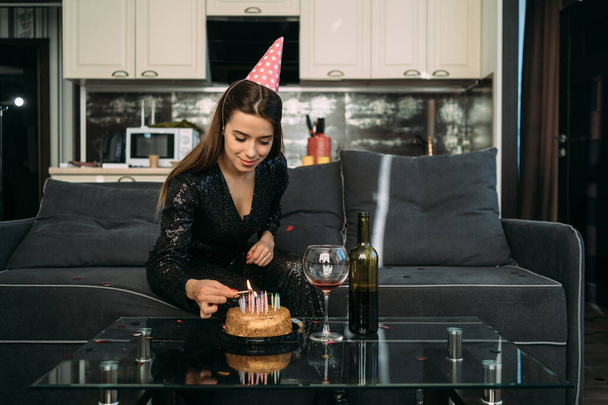 Narozeniny, žena zapaluje svíčky na dortu, kavkazská dívka ve slavnostní čepici doma, výročí vzdálenosti karantény, osamělá dovolená, narozeninová oslava koncepce doma - Fotografie, Obrázek