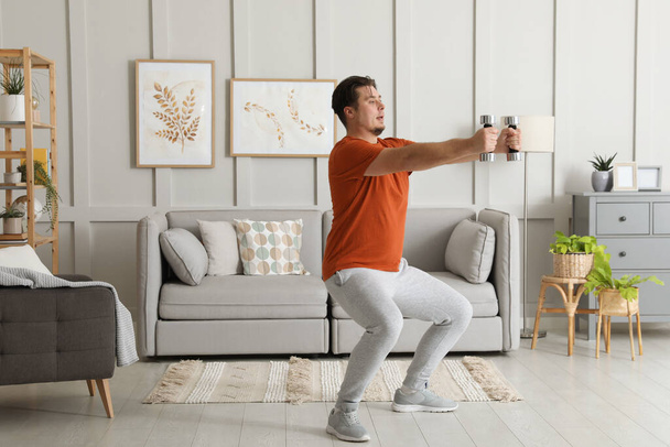 Υπέρβαρος άνθρωπος κάνει κατάληψη άσκηση με αλτήρες στο σπίτι - Φωτογραφία, εικόνα