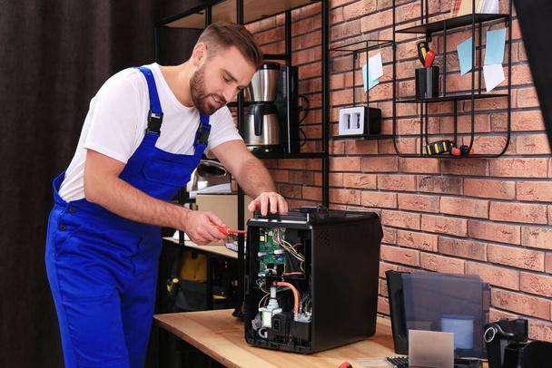 Repairman with screwdriver fixing coffee machine at table indoors - Photo, image