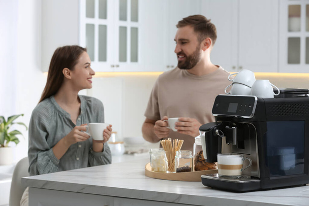 Happy couple enjoying fresh aromatic coffee in kitchen, focus on modern machine - Zdjęcie, obraz